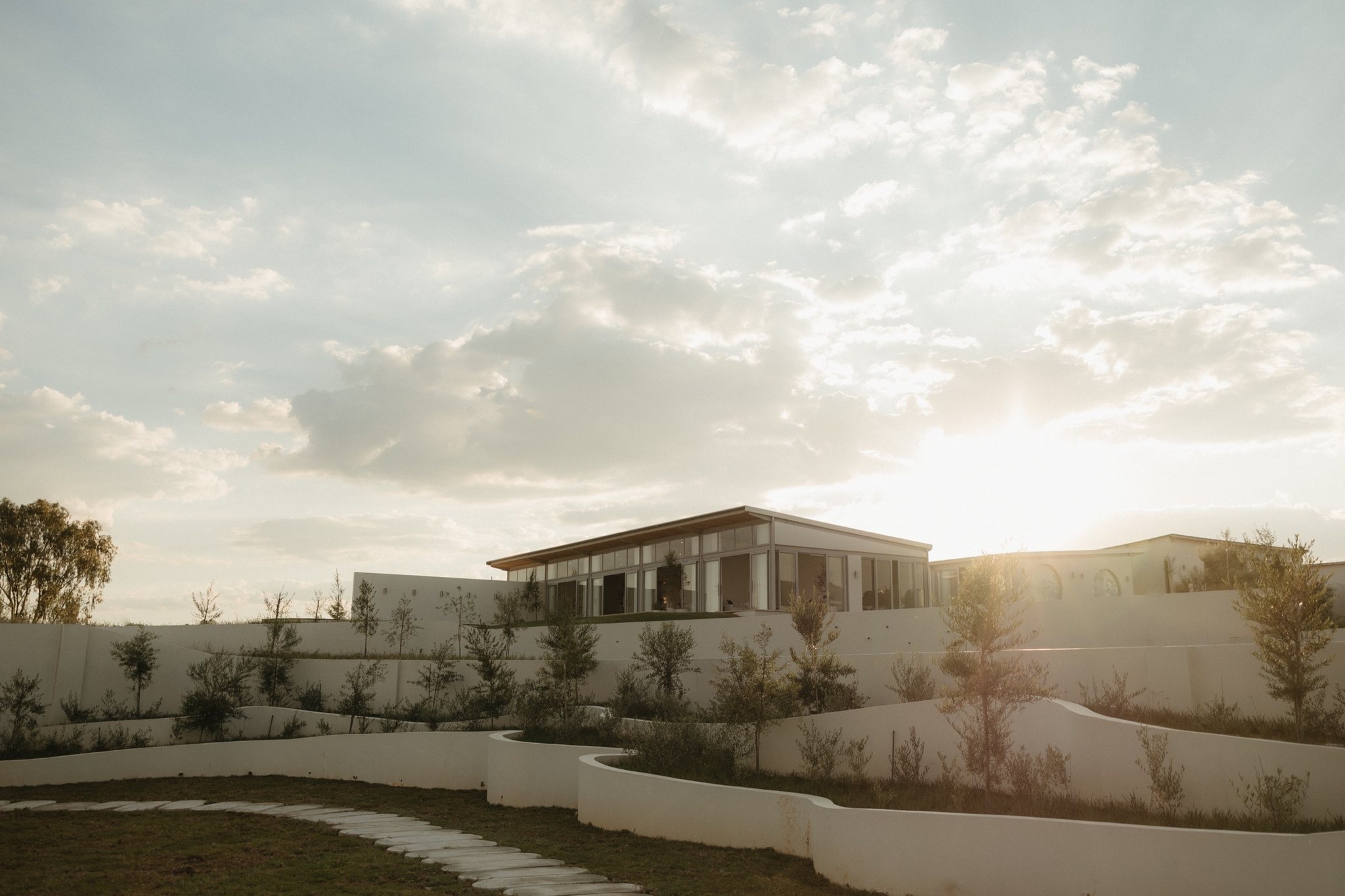 The white curved pavilion of STAY at golden hour, the sun setting behind low white walls and open veld