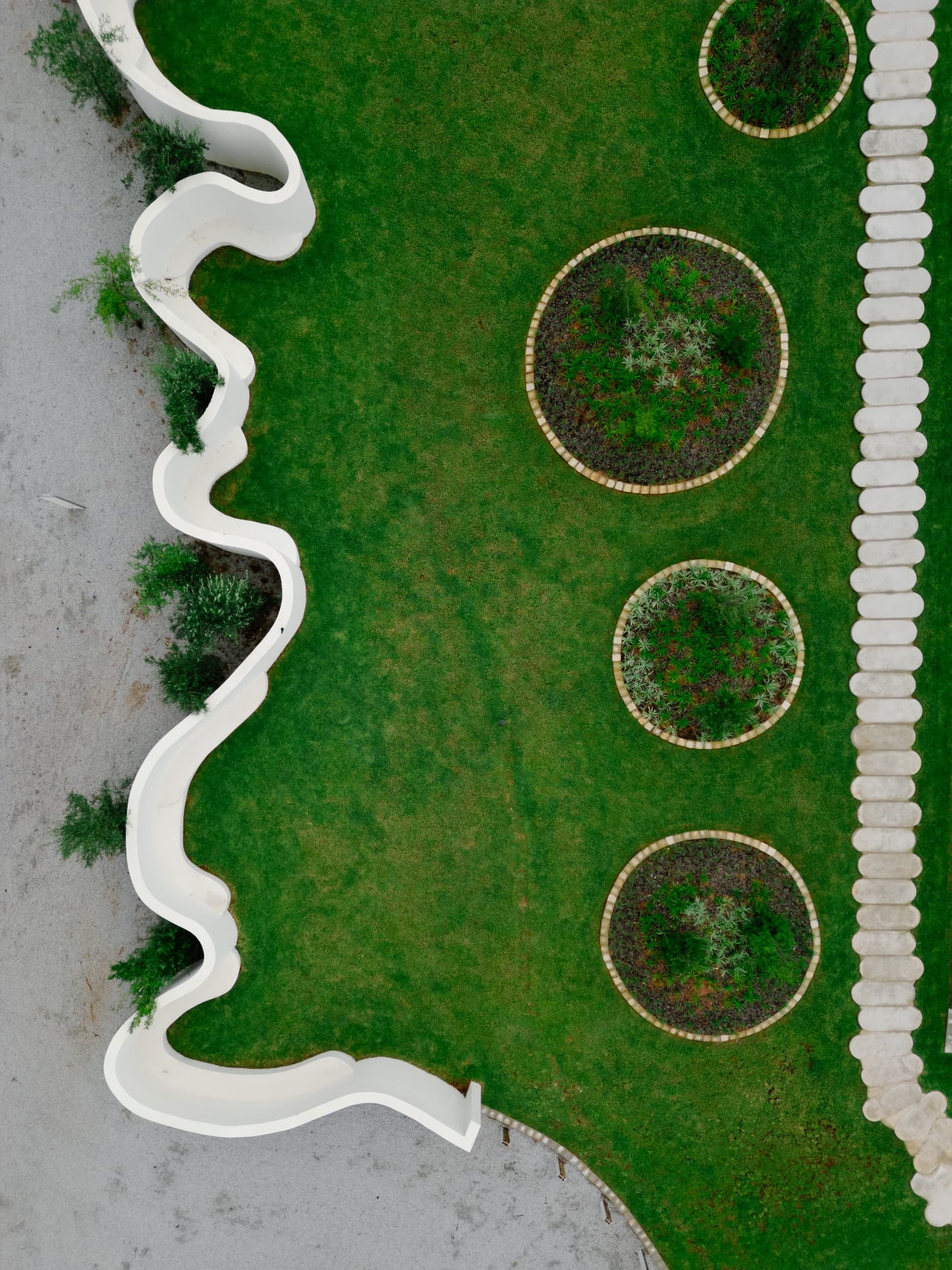 The white curved pavilion of STAY beyond a low white wall and young indigenous planting